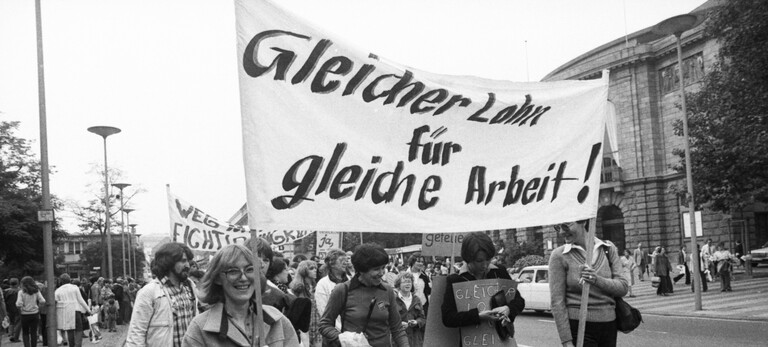 Frauen und Maenner demonstrieren gegen Lohndiskriminierung, Auf einem Plakat steht ' Gleicher Lohn für gleiche Arbeit!'